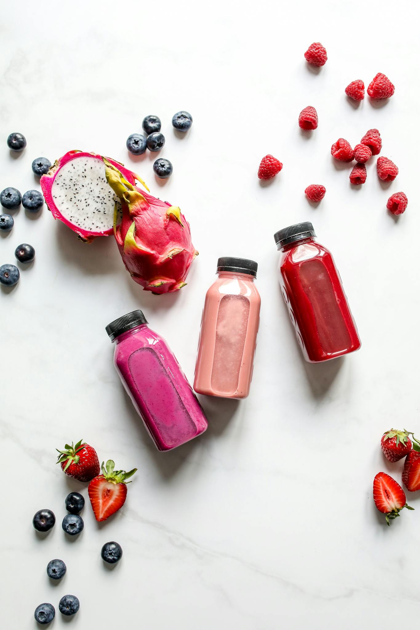 Colorful fruit smoothies with dragon fruit, berries, and more on a white background.