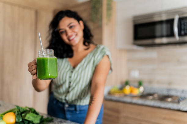 Close up of woman holding a glass of detox juice in kitchen at home